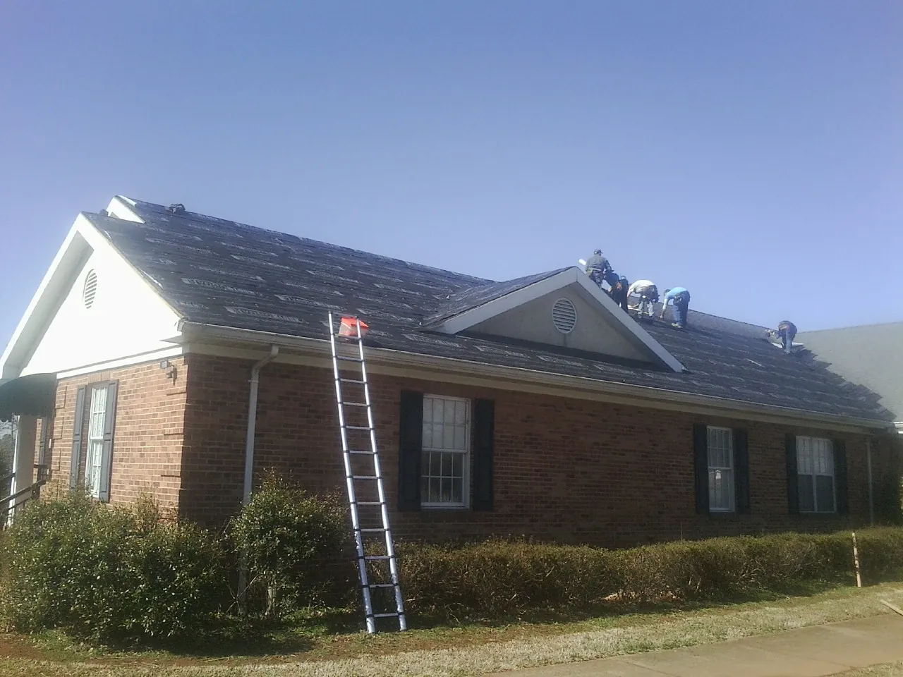 Crew tearing shingles off a brick ranch roof with a ladder set — Emergency Roof Repair work by our crew in Big Indian