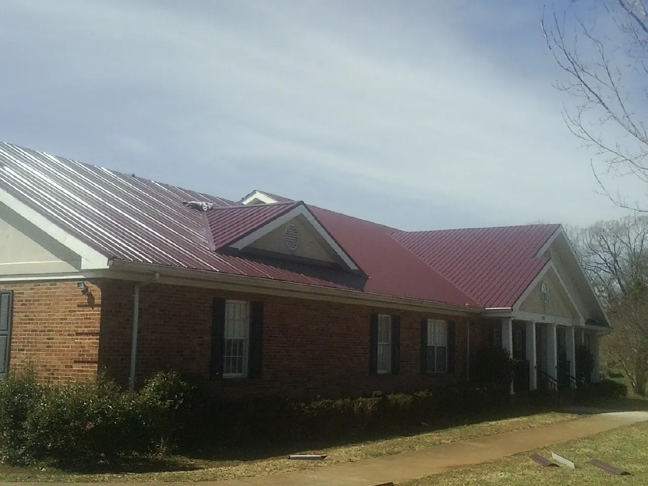 Red metal roof with gabled entries on a long brick building, from a Hail Damage Roof Repair job in Big Indian