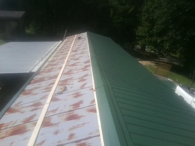 Old rusted panels beside newly installed green metal roofing — Wind Damage Roof Repair by Roofing Brothers in Big Indian