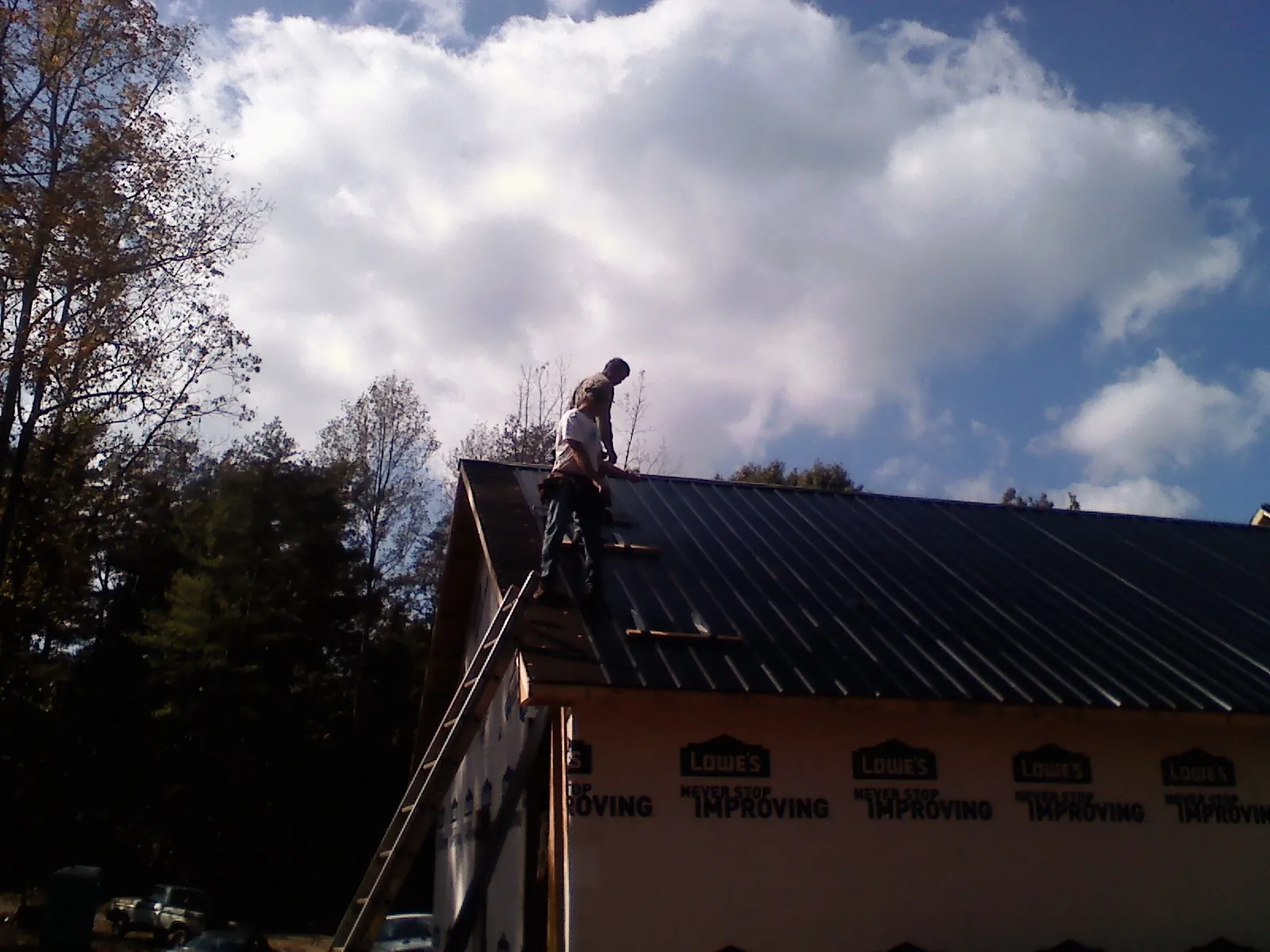 Roofer fastening dark metal panels high against a cloudy sky, from a Roof Inspection job in Big Indian