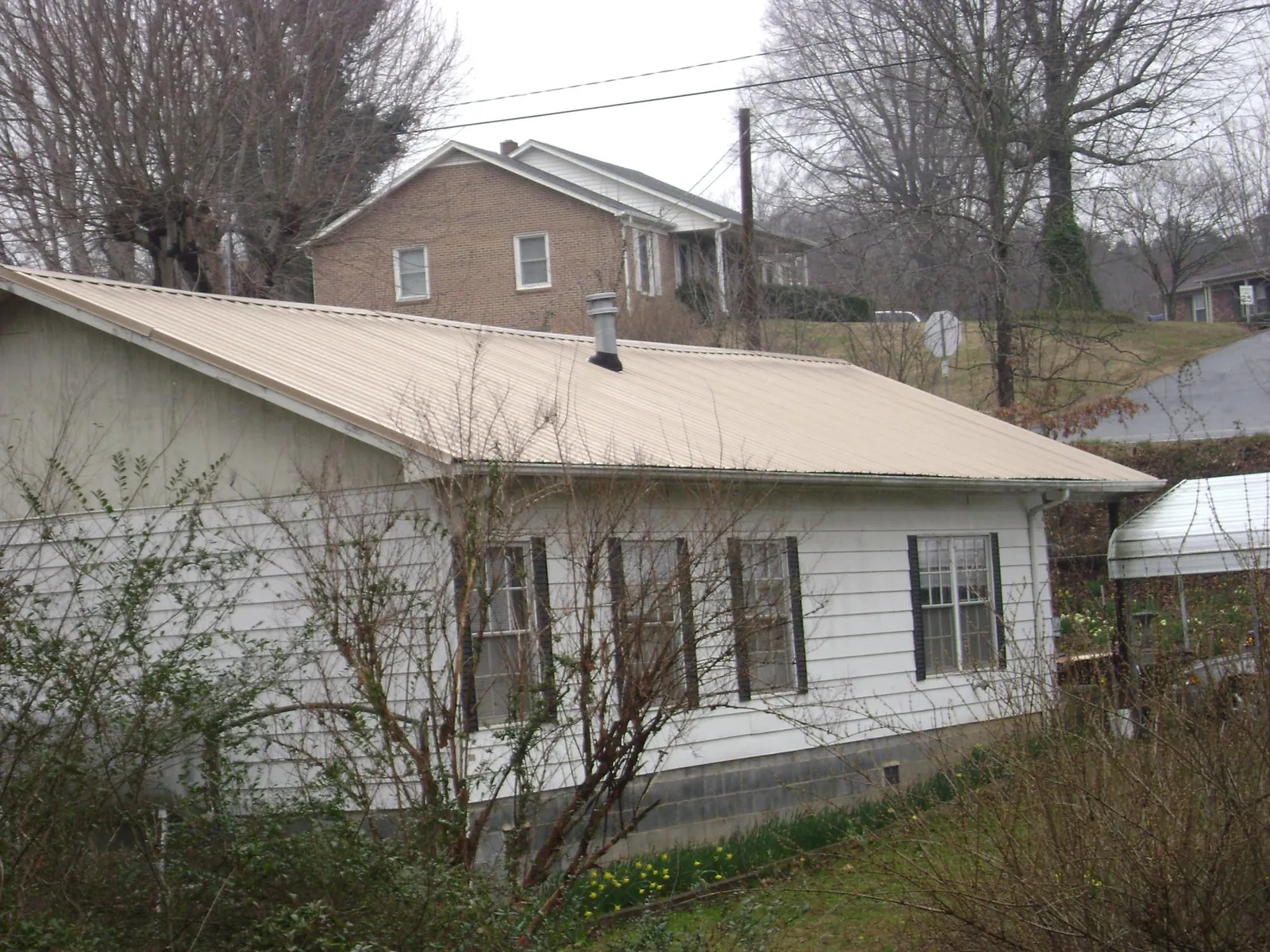 Tan metal roof on a white sided house set into a hillside — Commercial Roofing by Roofing Brothers in Big Indian
